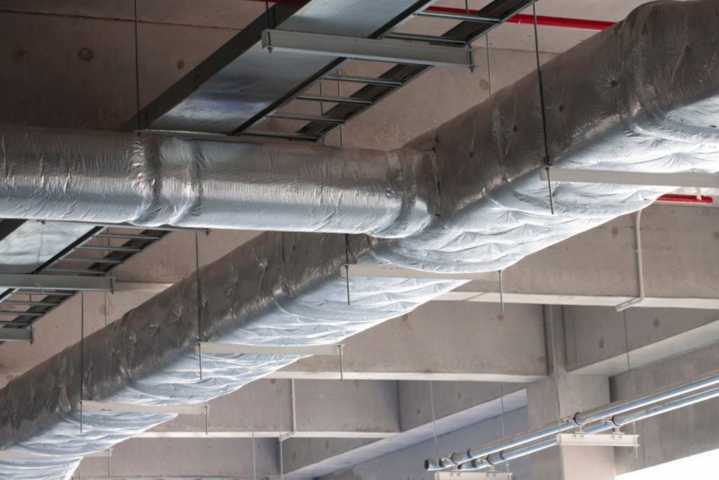 Industrial building interior featuring a network of pipes and ducts along the ceiling and walls.