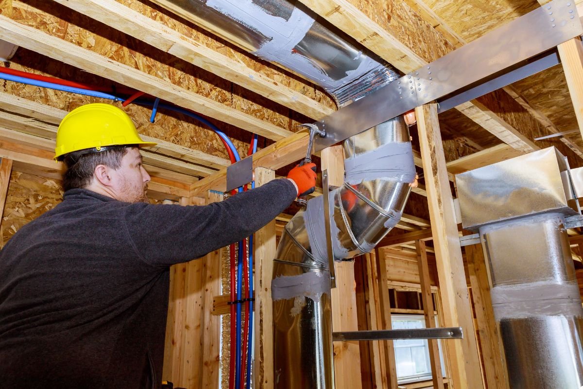 A man in safety gear, including a hard hat and glasses, is focused on repairing.