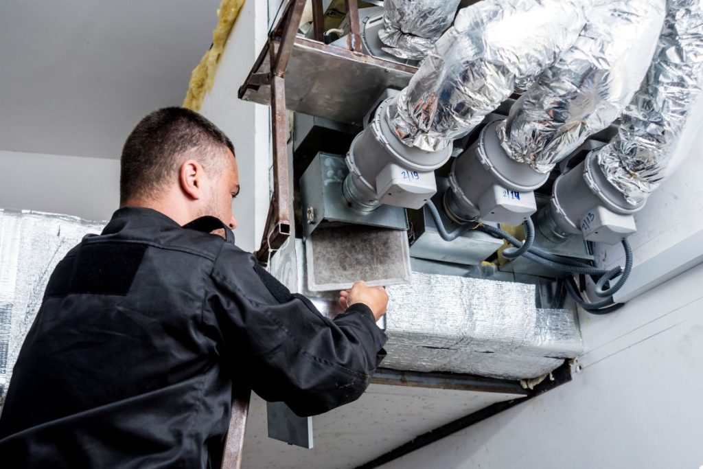 A man wearing a black shirt is engaged in maintenance work on a furnace in a well-lit workshop.