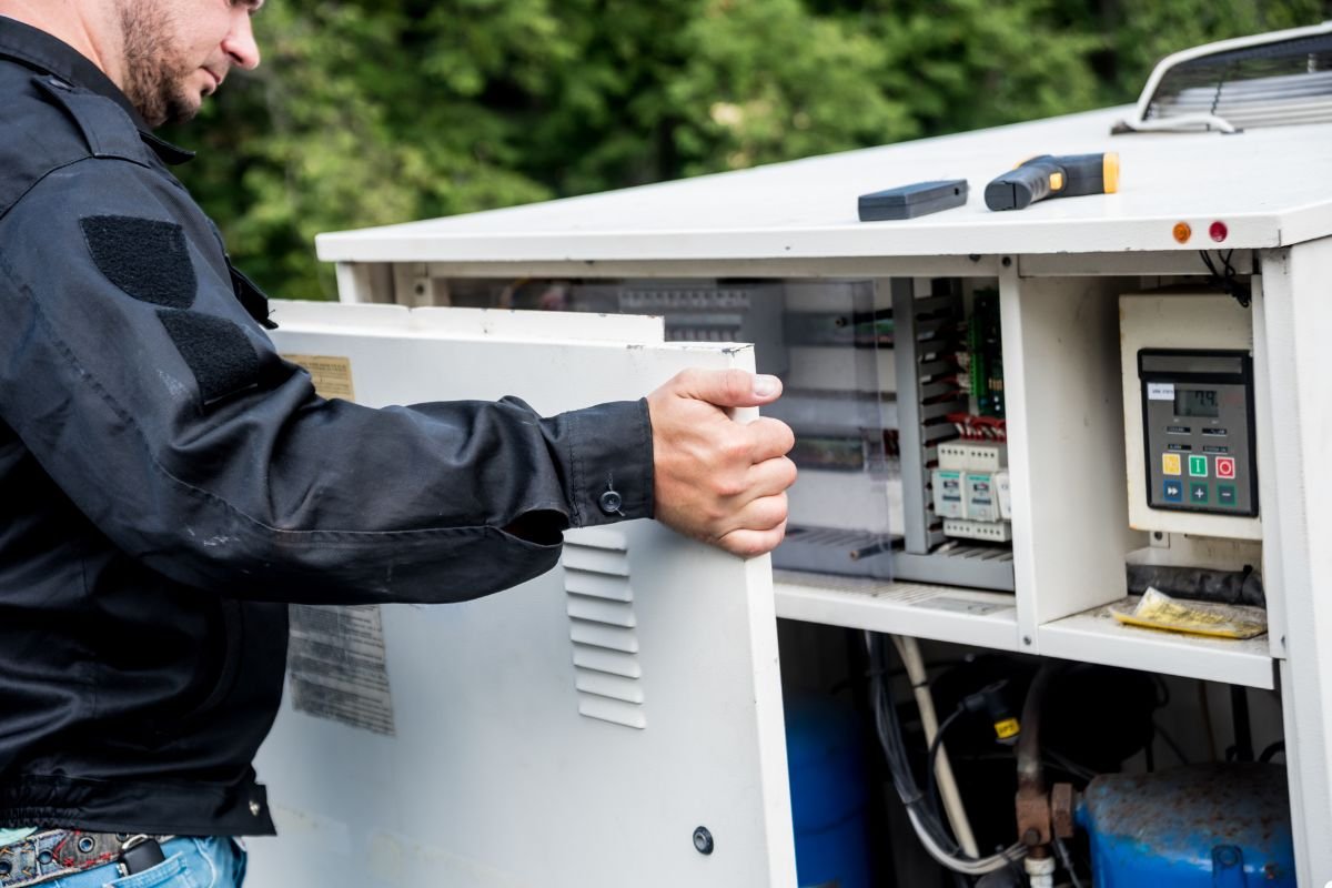A man is opening the door of a portable air conditioner, preparing to access its internal components for maintenance.