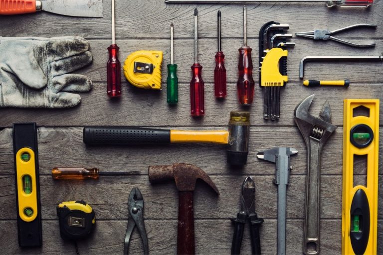 Tools of different types laid out on a wooden table, featuring drills, screwdrivers, and a toolbox.