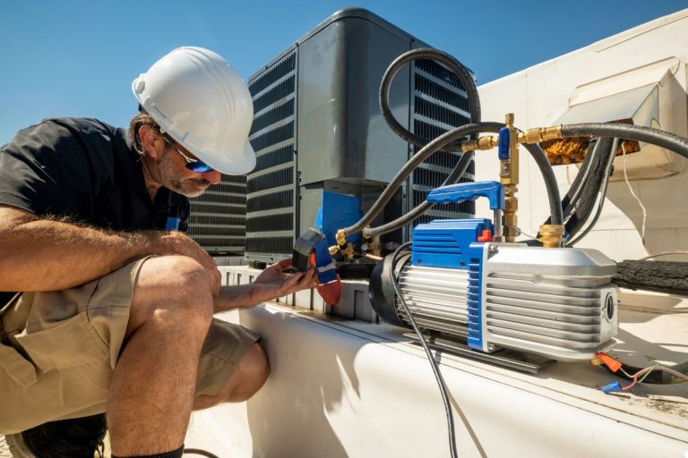 A man repairs an air conditioning unit, focused on his work with tools in hand and the unit open for maintenance.