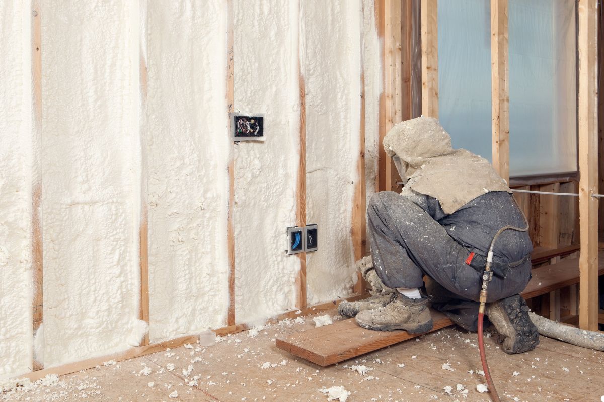 A man in a white jacket and hat is focused on repairing a wall.
